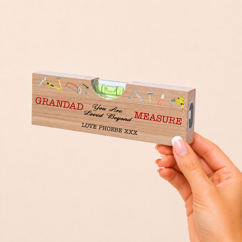 Hand holding a wooden ruler with engraved text and tools on a beige background
