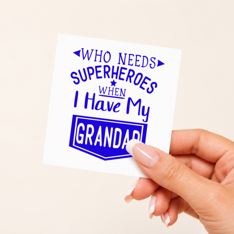 Hand holding a card with text 'WHO NEEDS SUPERHEROES WHEN I HAVE MY GRANDAD' on a beige background