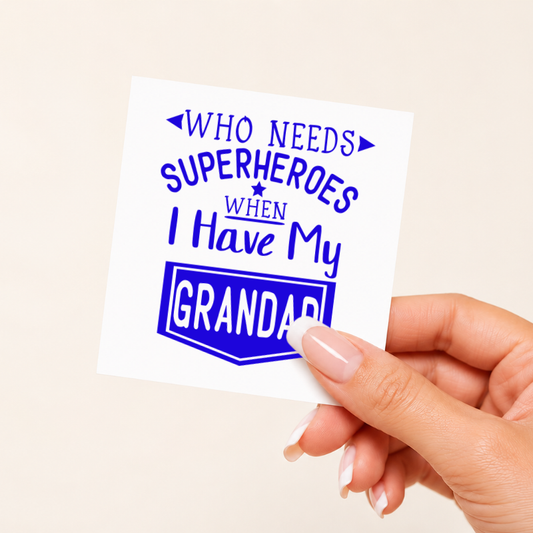 Hand holding a card with text 'WHO NEEDS SUPERHEROES WHEN I HAVE MY GRANDAD' on a beige background